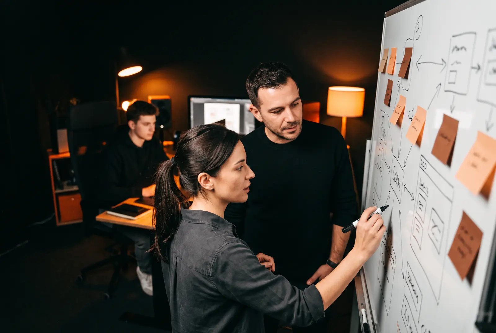 Two teammates sketch app screens on a whiteboard covered in sticky notes